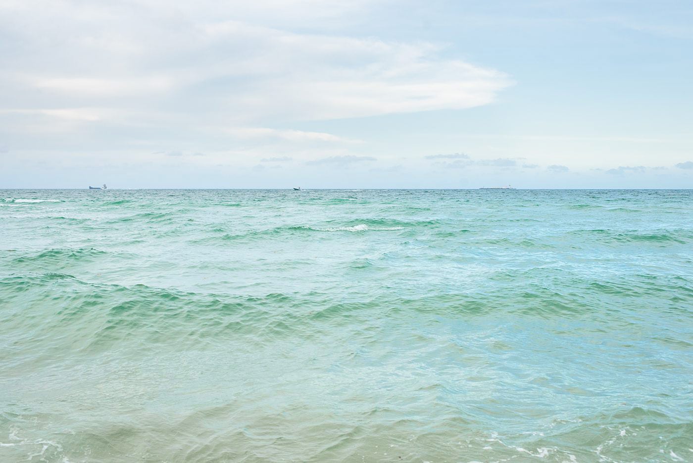 Lightly colored turquoise ocean water with a light blue sky above it.