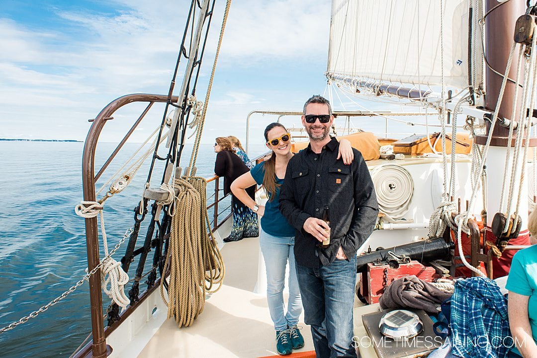 A smiling couple on a sailboat with blue skies and water.