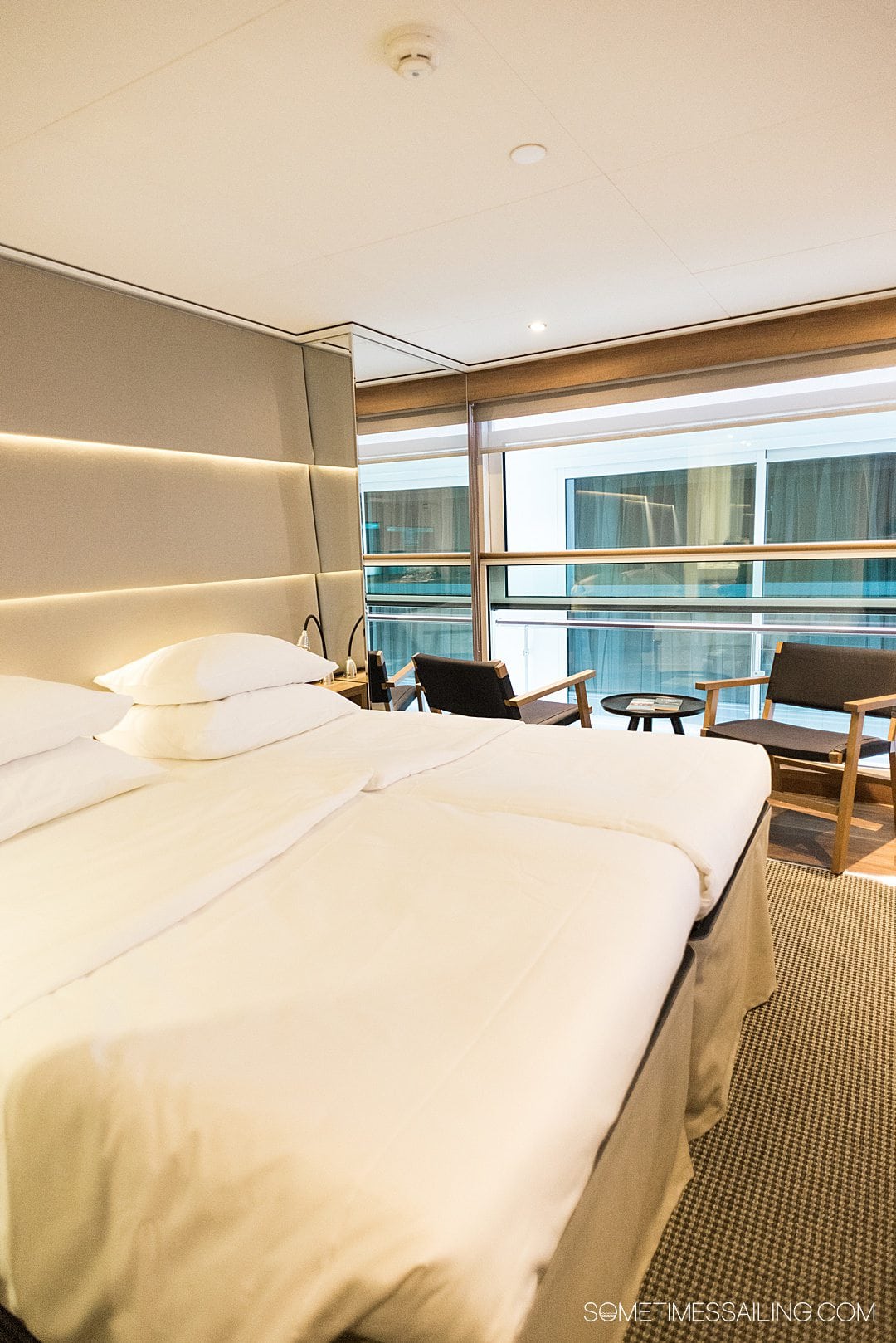 Cabin interior on an Emerald Cruises river cruise ship. A bed with white linens and pillows and glass window in the distance.