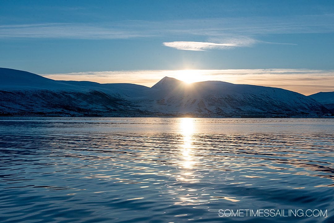 The sun sets over snowy mountains in Tromso, Norway as seen on the fjord during a polar boat cruise.