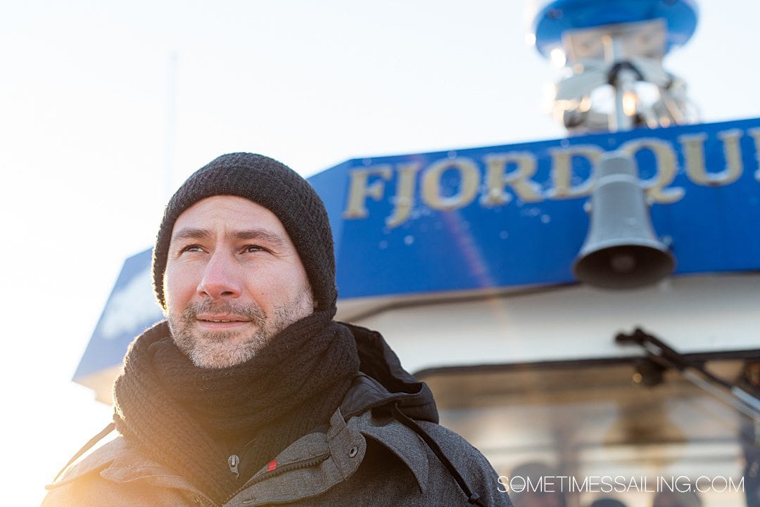 A man in front of the windshield of a boat with "Fjord" letters above.