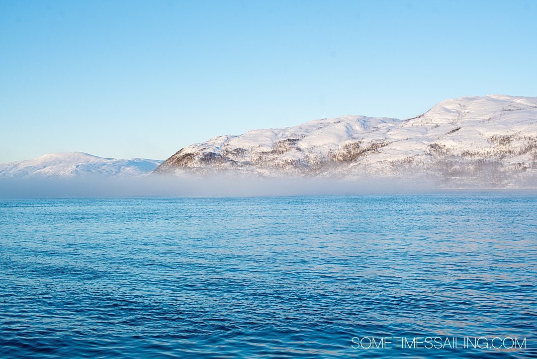 Blue water and snowy mountains with mist above the ocean on a Tromso, Norway boat tour.
