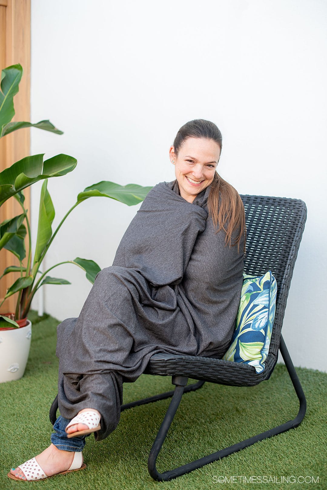 Woman on a chair wrapped in a grey blanket that converts from a scarf, for best cruise gifts.