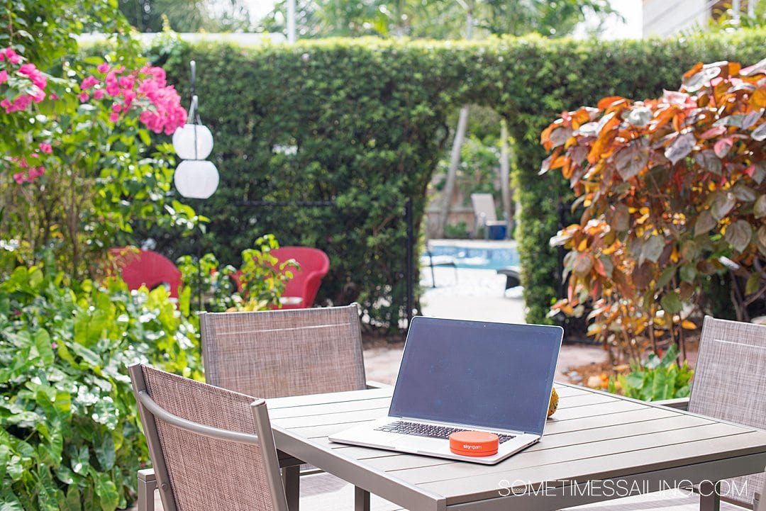 Laptop on a table with a round orange circle hotspot on it, and tropical greenery in the background.