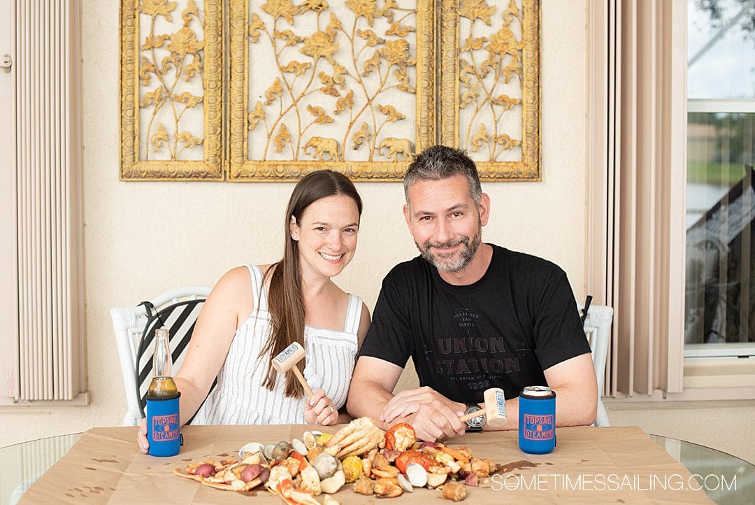 Man and woman at a table covered in brown kraft paper with the contents of seafood steamer pots laid out for lunch.