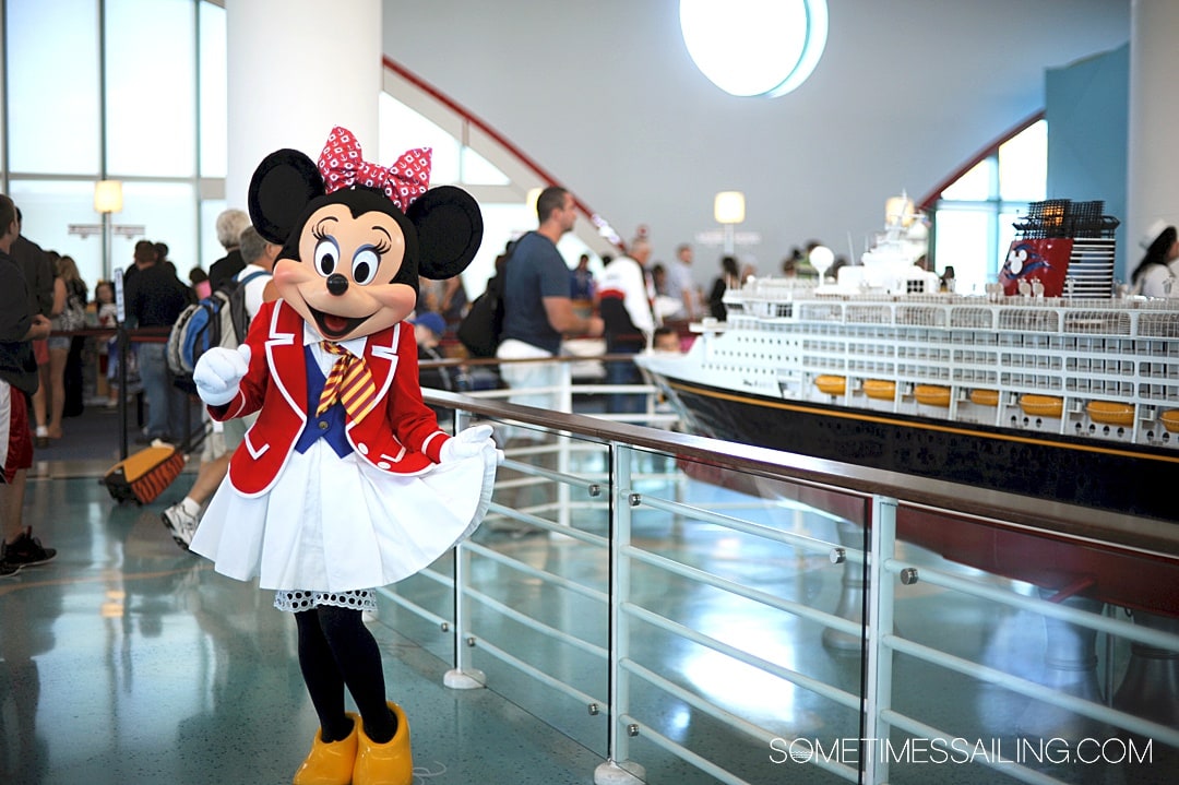 Minnie Mouse in a sailor outfit in front of a scale model of the Disney Cruise Line ship.