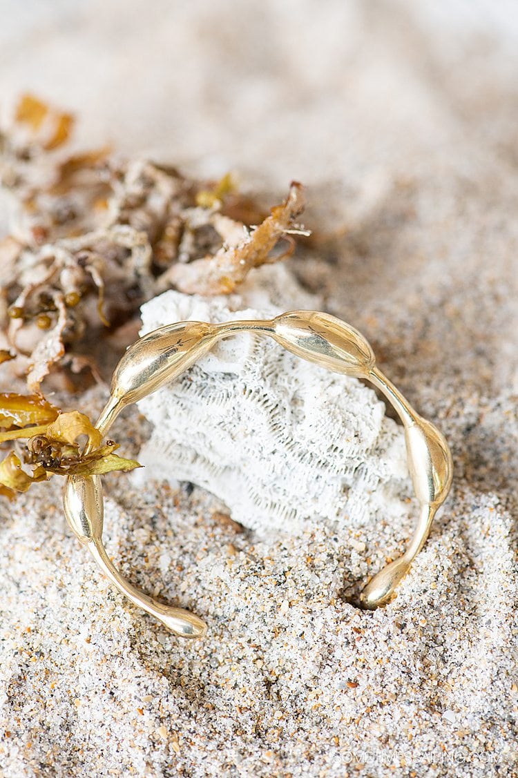 Brass seaweed inspired bracelet by Wildwood Oyster Co. on a piece of coral and sand.