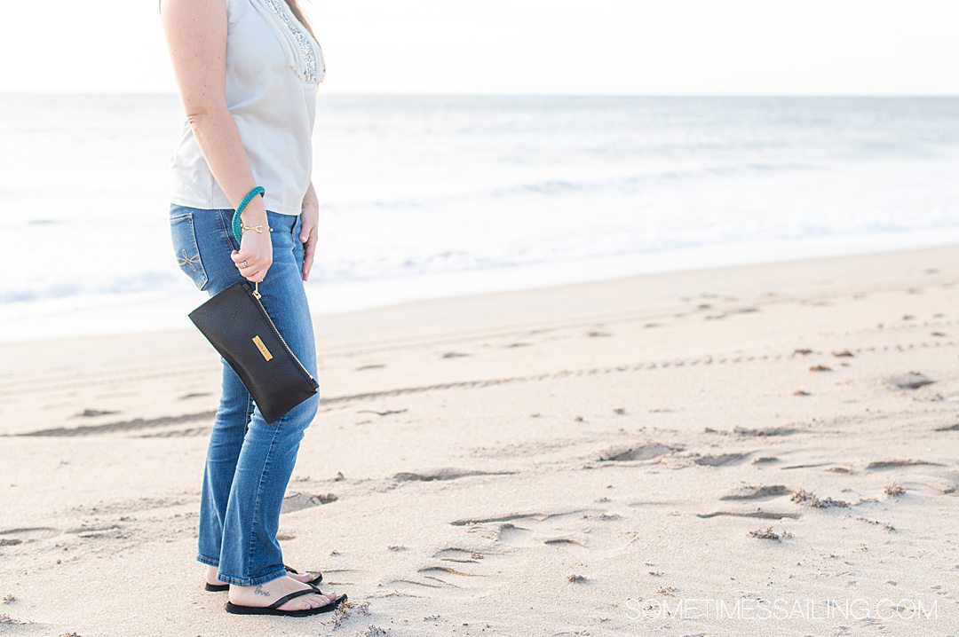 Woman holding a black leather clutch on the beach.