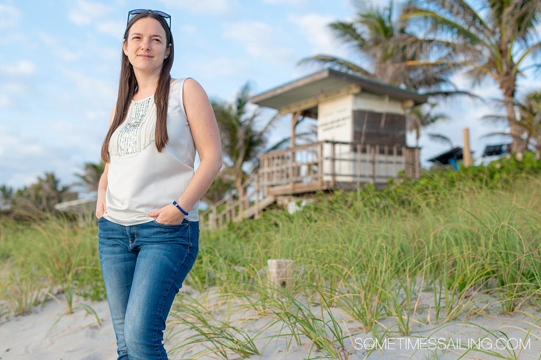 Woman wearing an OMEGA sailing bracelet with a beach dune and grasses, and blue sky behind her.