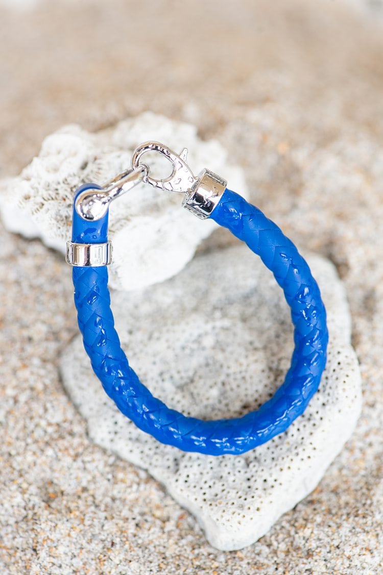 Blue rubber and stainless steel sailing bracelet from OMEGA against sand on the beach and a piece of white coral.