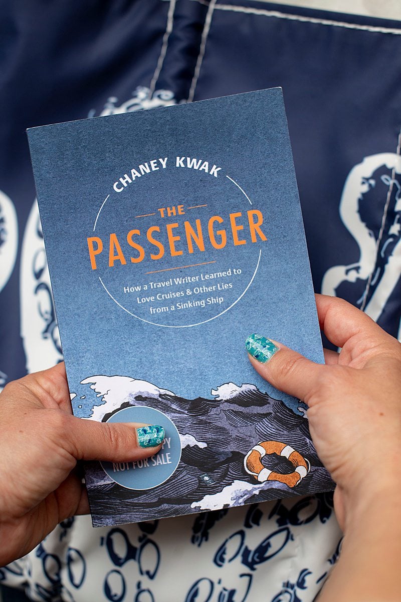 Book The Passenger with a blue cover, held in front of a bag with octopus tentacles for a post about non-fiction cruise books.