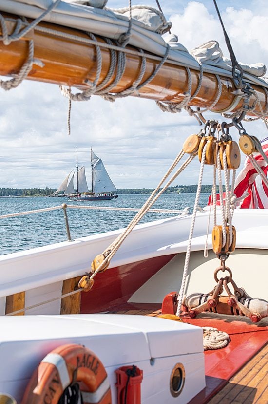 Looking inside a boat on pulley strings and with a sailboat in the distance, part of Maine Windjammer Association's fleet.