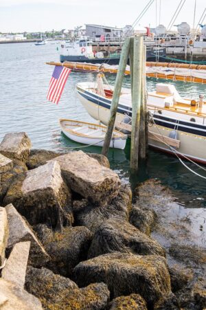 American Eagle schooner in the port of Rockland, Maine with rocks on the left and the back of the ship on the right, with a rowboat in the water.