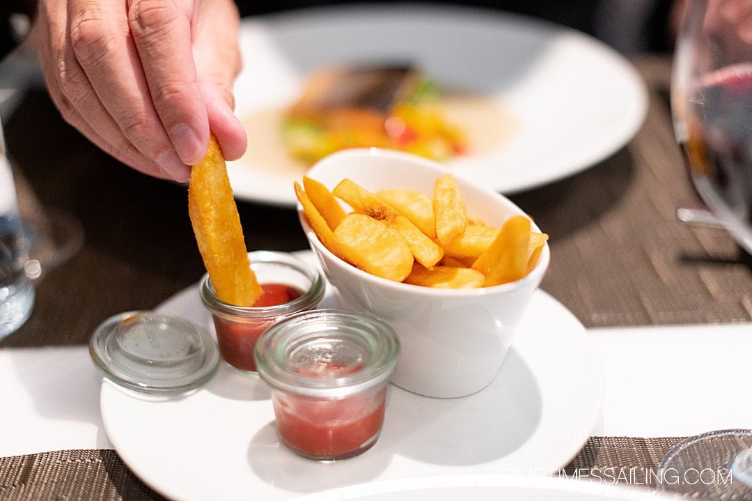 Oval dish of steak French fries with a hand dipping a fry into ketchup on the Emerald Destiny river cruise ship.
