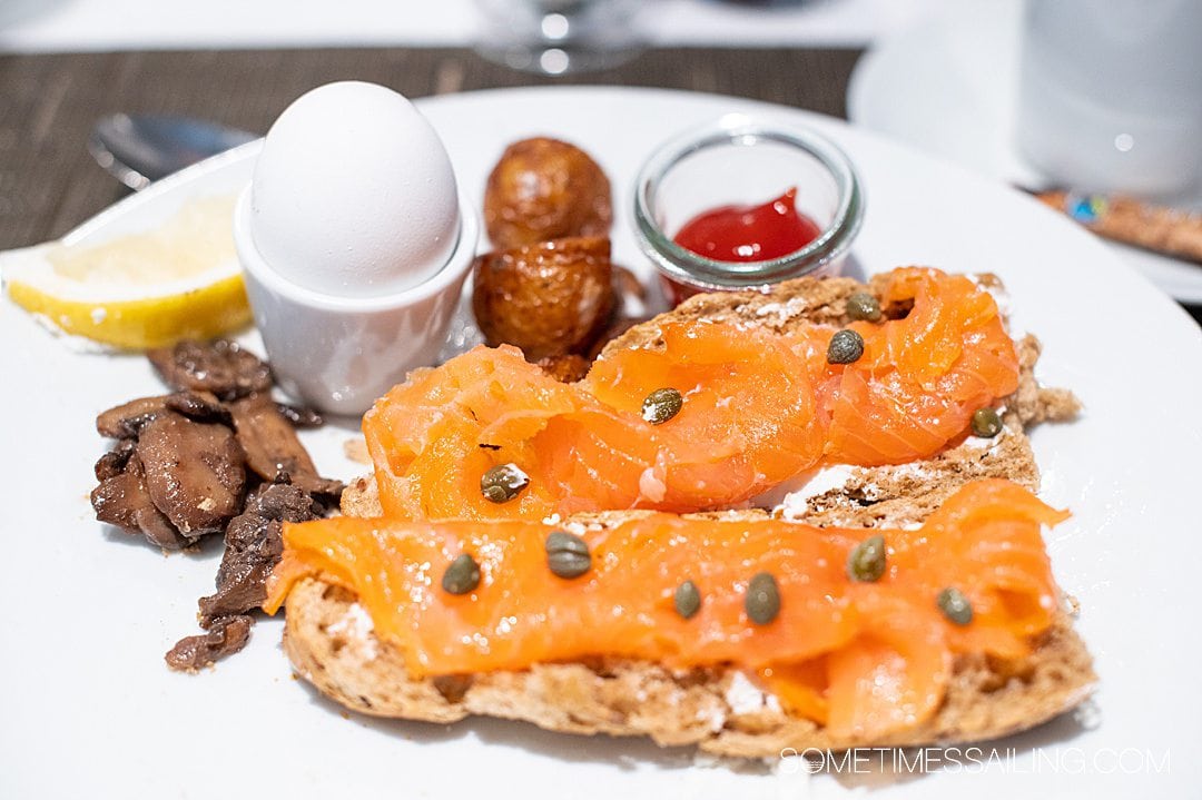 Bread with smoked salmon with capers on top, on a plate with a hard boiled egg, sauteed mushrooms, and potatoes on Emerald Destiny river cruise ship.