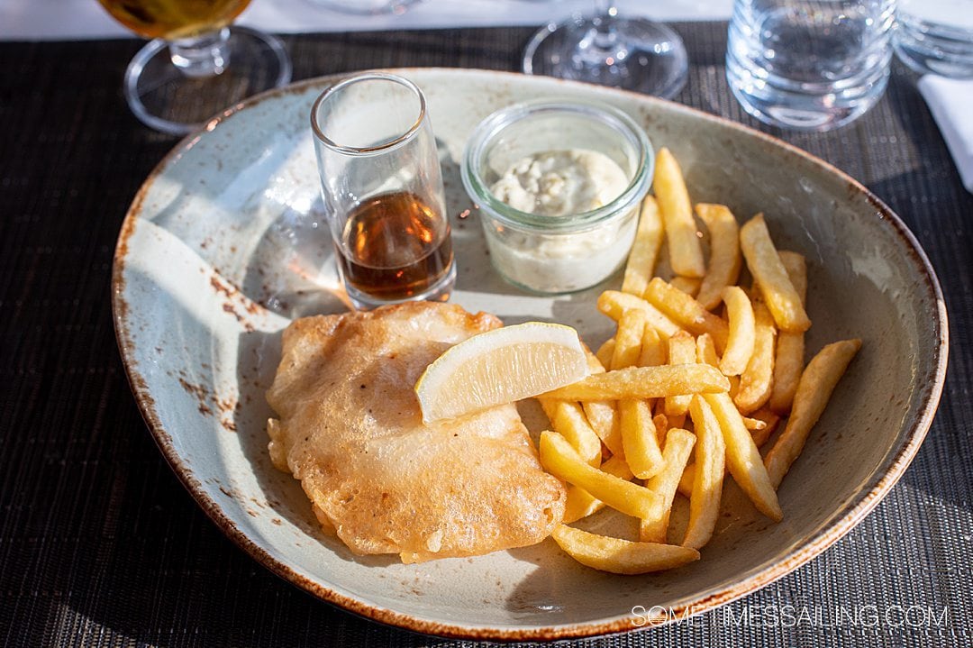 Blue plate of fish and chips and a side of malt vinegar and tartar sauce on Emerald Destiny river cruise ship.
