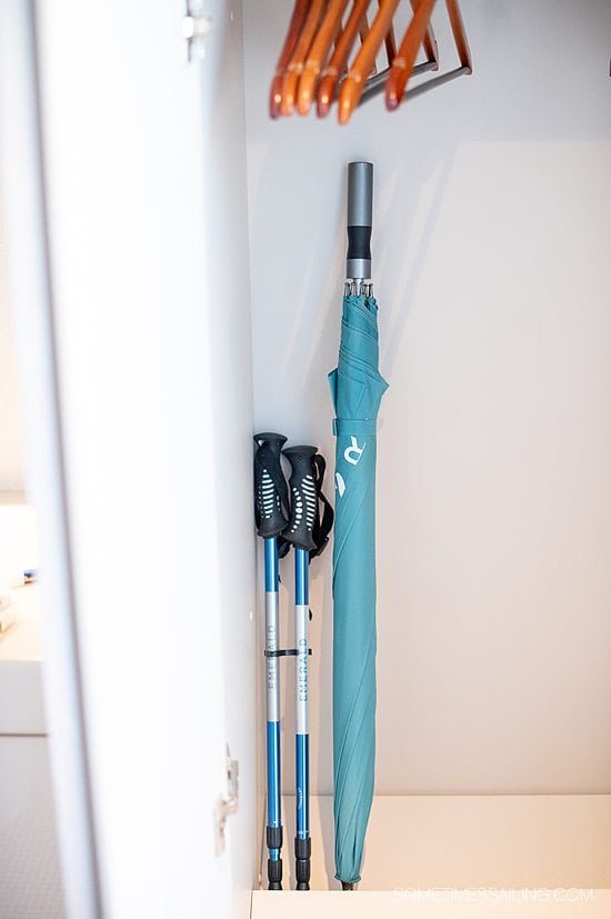 Blue-green umbrella collapsed and standing upright in a closet on Emerald Destiny next to aluminum walking sticks.