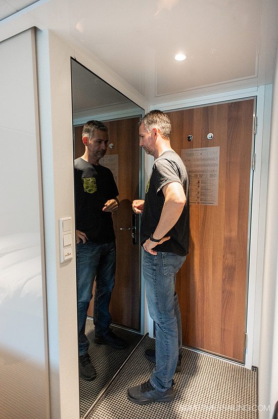 Man looking in the mirror behind the door of a stateroom on Emerald Destiny river cruise ship.