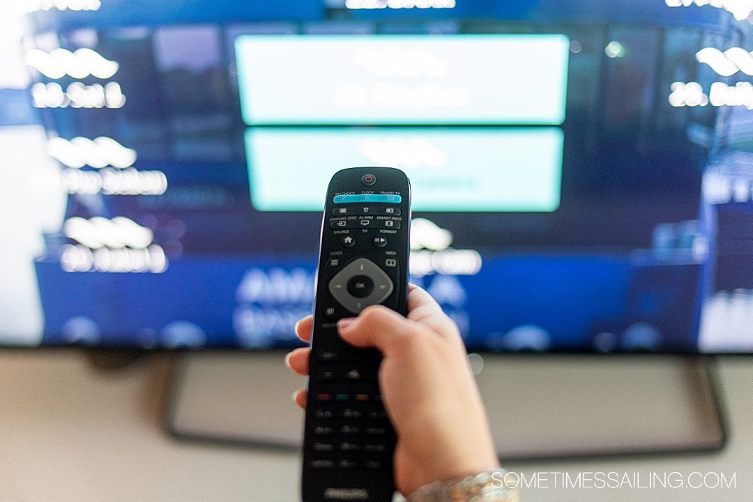 Woman's right hand on a black remote control and blurry tv screen in the background.
