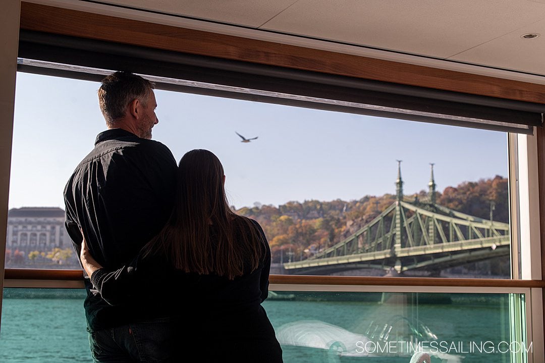 Couple looking out at a bridge in Budapest, in their Emerald Destiny cabin on a river cruise.