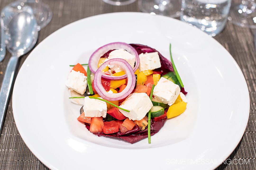 Colorful Greek salad on Emerald Destiny river cruise ship, with feta cheese blocks, sliced red onion, yellow peppers, red tomatoes and green chives. 