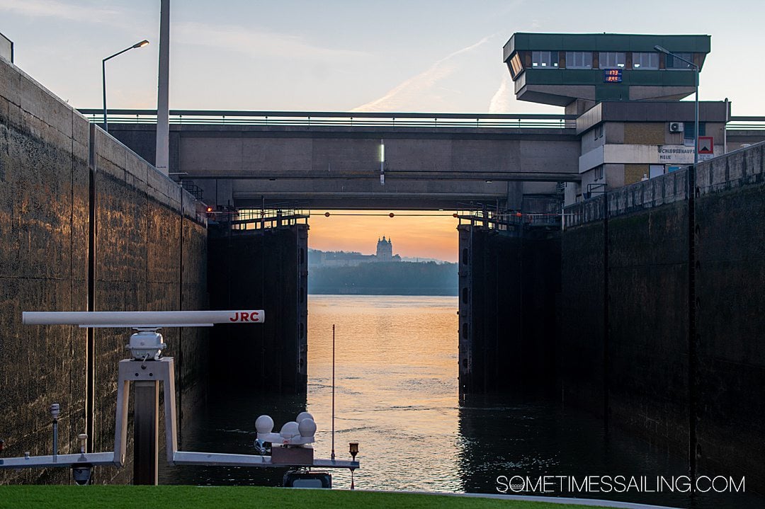 Doors to a river lock opening to reveal a sunrise and building in the distance.