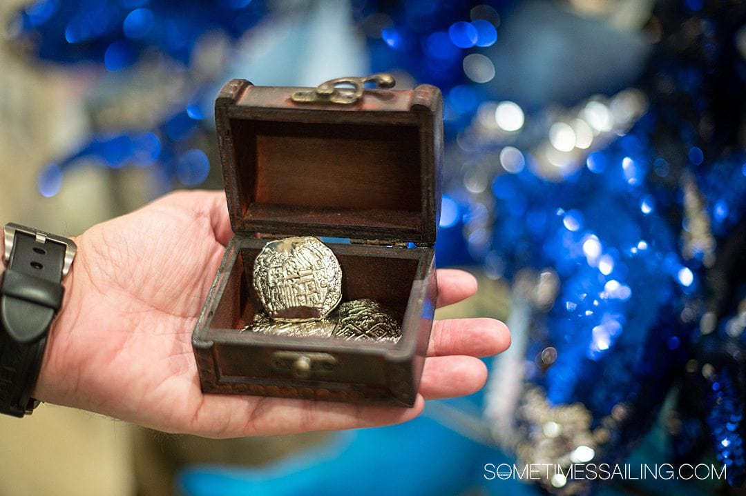 Man's hand holding a small treasure chest with a gold coin in it for a surprise cruise reveal ideas.