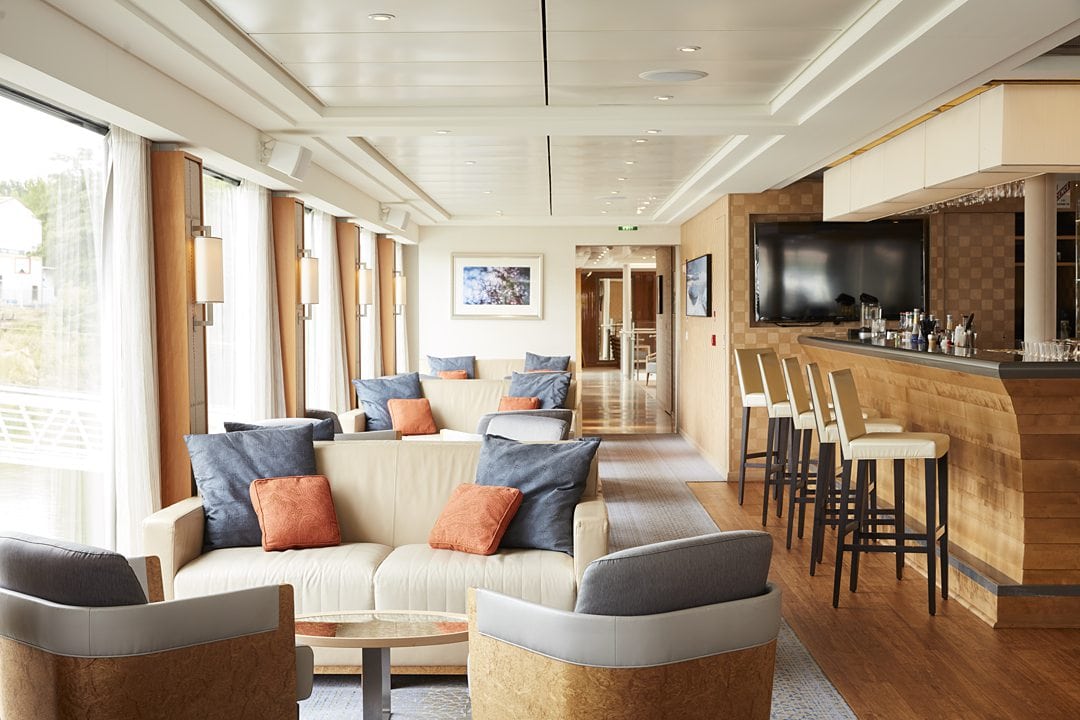 Lounge are with couches and a bar on the right with bar stool on a Viking Longship river cruise in Europe.