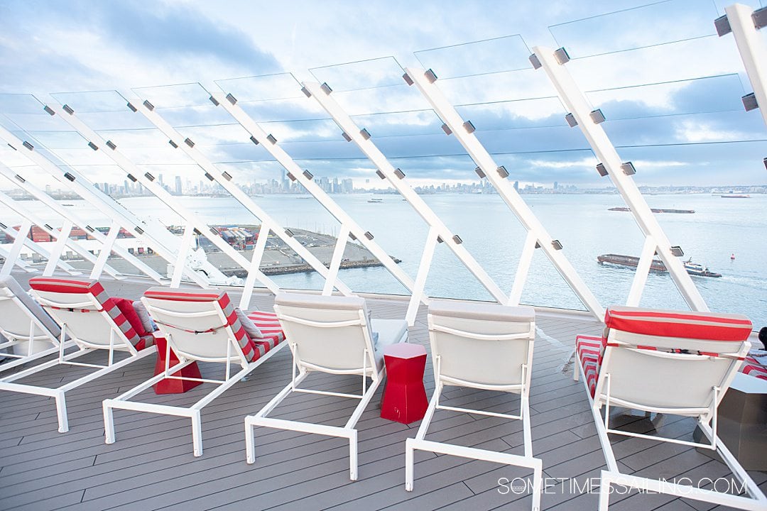 Lounge chairs on the top deck of a cruise ship, with the NYC skyline in the background.
