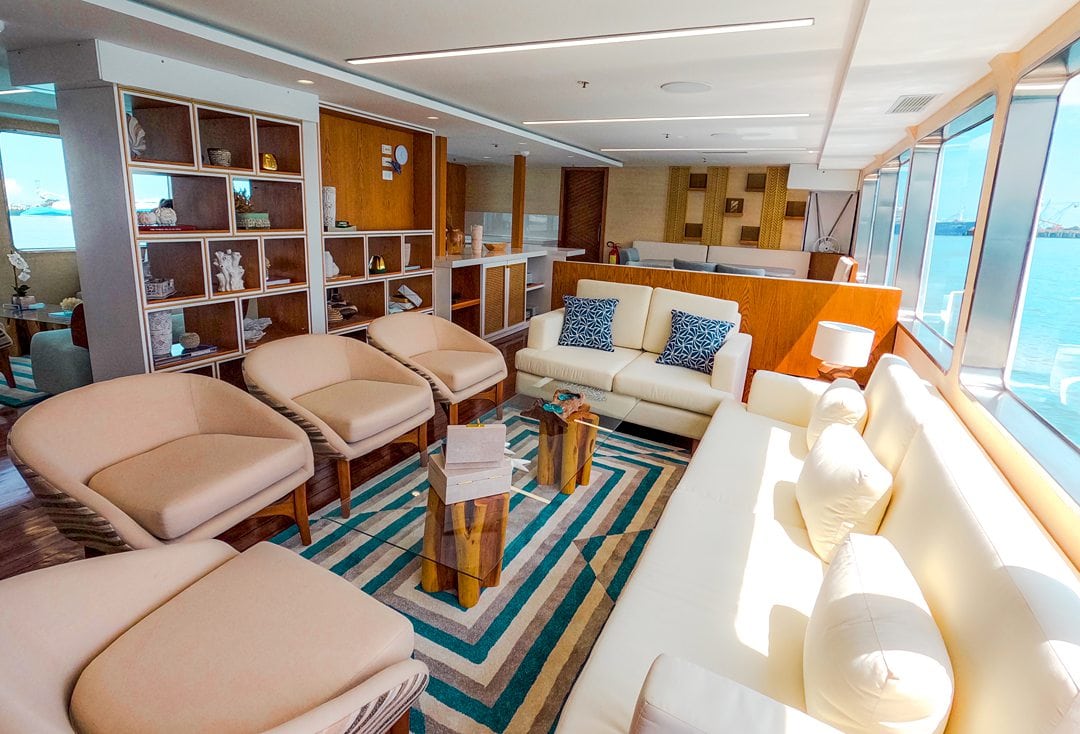 Interior lounge space of Kontiki Expeditions yacht cruise ship, with neutral color furniture and a blue-tone rug, which sails the coast of Ecuador.