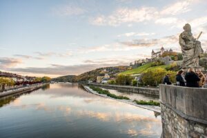 Sunset reflection on the Main River, with a green hillside and fortress to the right for a post about European River Cruises.