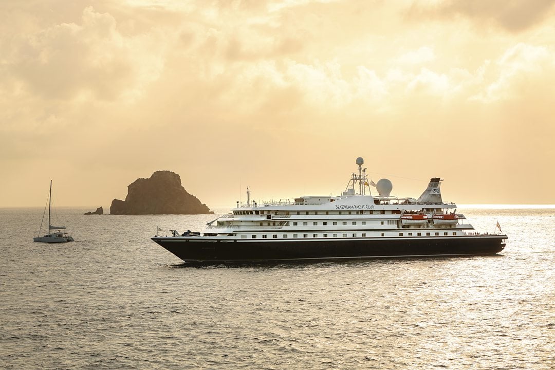 Sunset with an orange-yellow sky above a SeaDream Yacht Cruise ship in the water.