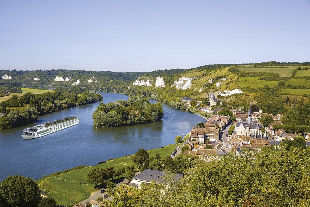 Aerial view of an Emerald Cruises river cruise ship on the left with a green European port on the right.