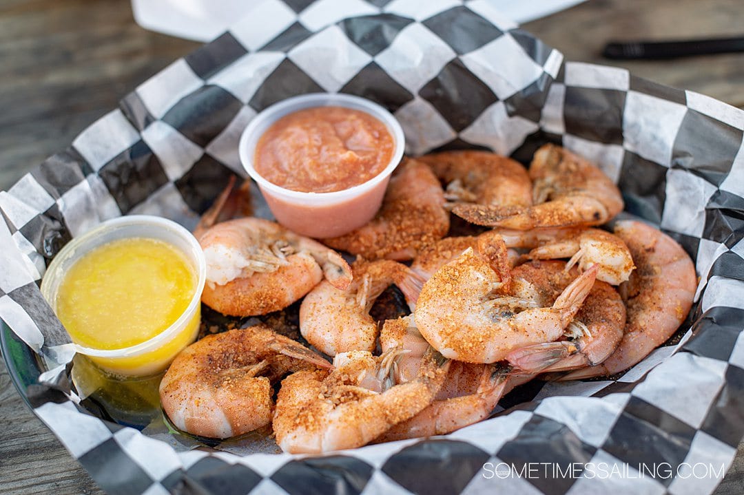 Seasoned steamed shrimp in a basket on black and white checkered paper with a container of melted butter and cocktail sauce.