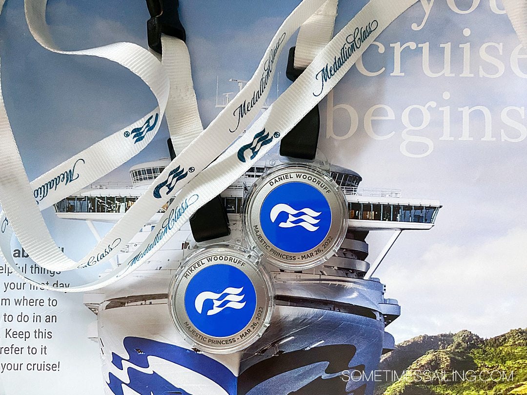 Princess Medallion devices with a white lanyard wrapped around them against a photo of a cruise ship.