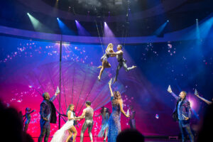 Cruise ship entertainment on Celebrity Apex with acrobatics for Crystallize and a colorful background with pink and purple colors.