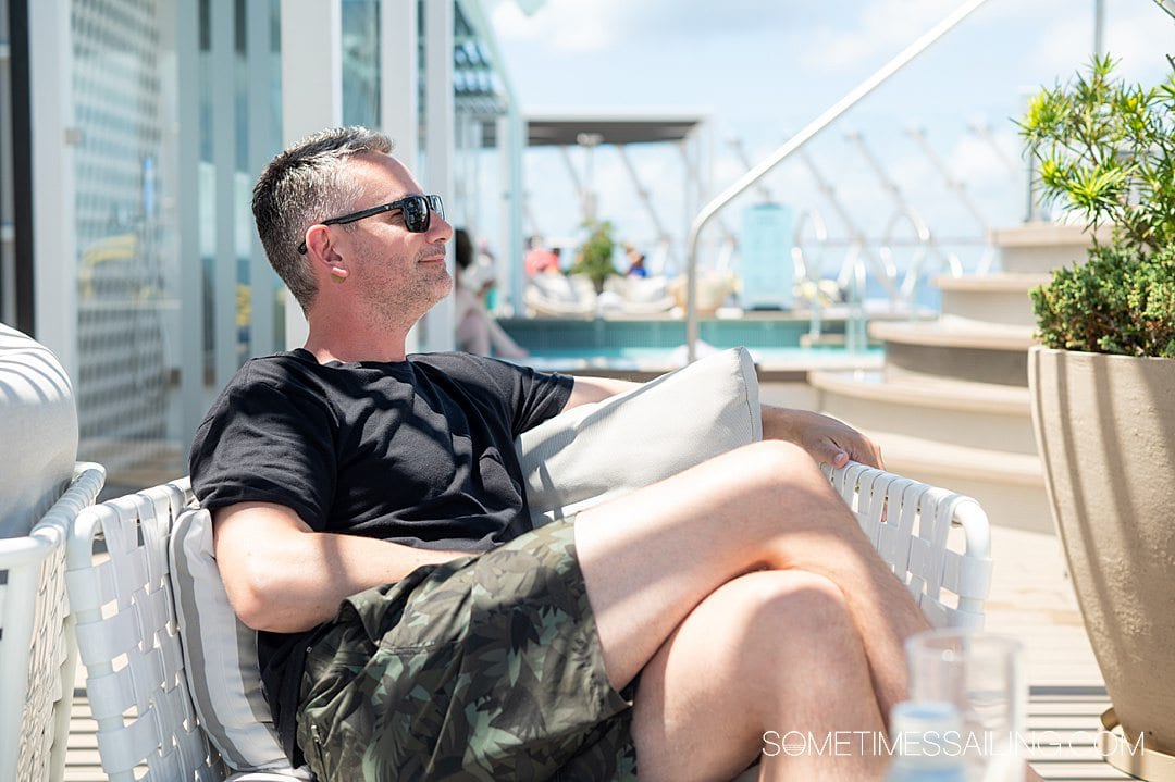 Profile view of a man sitting on a chair with a small skin-tone dot behind his ear, which his a motion sickness patch for anti-nausea if you get sea sick on a cruise. 