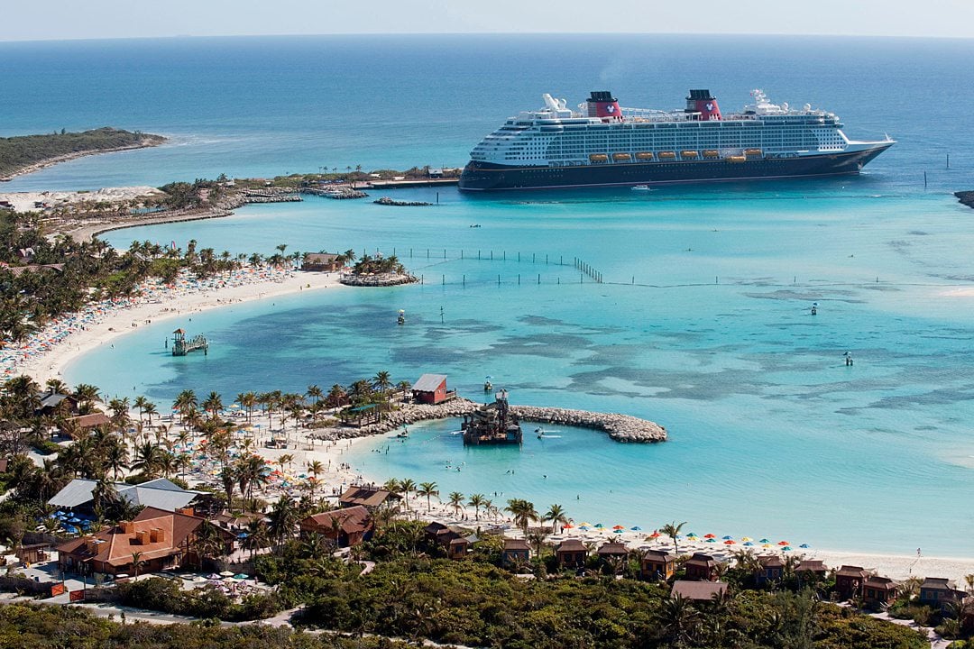 Disney Dream docked in the distance in an aerial view of Disney Cruise Line's Castaway Cay with turquoise water.