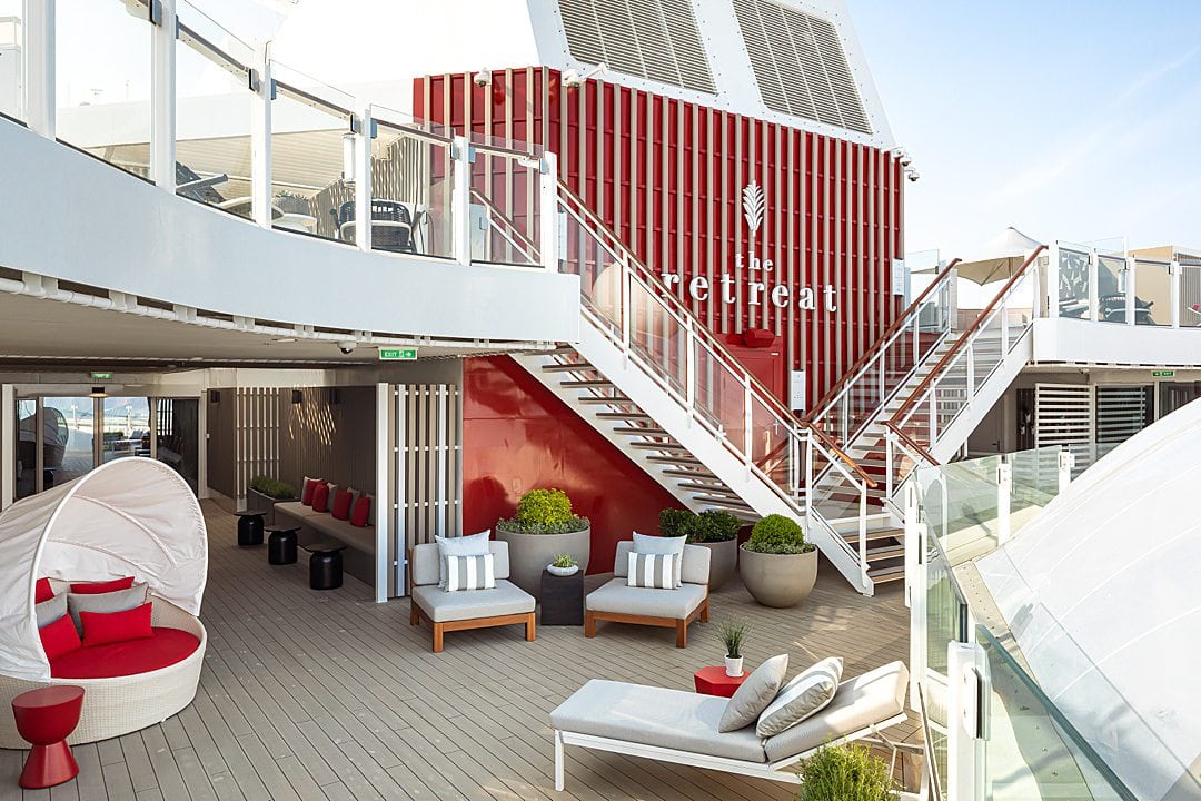 Red and white striped wall with a double white staircae leading to a deck with lounge chairs on The Retreat Sundeck on Celebrity Beyond.