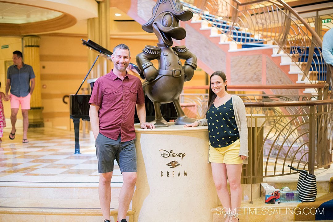Man and woman on the inside of a Disney Cruise ship by a Donald Duck statue.