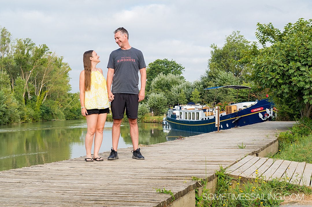 Couple looking at each other in front of a canal with a barge cruise boat in the background.