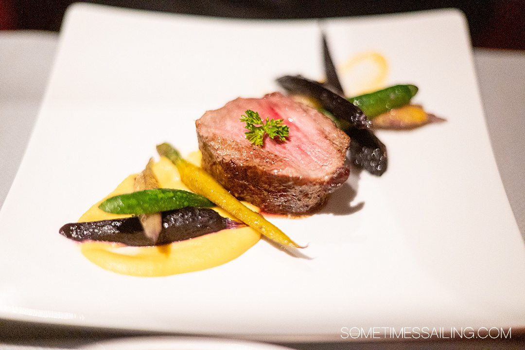 Entree of a slice of meat with diagonally placed colorful carrots and zucchini at Luminae in The Retreat on Celebrity Cruises ship.