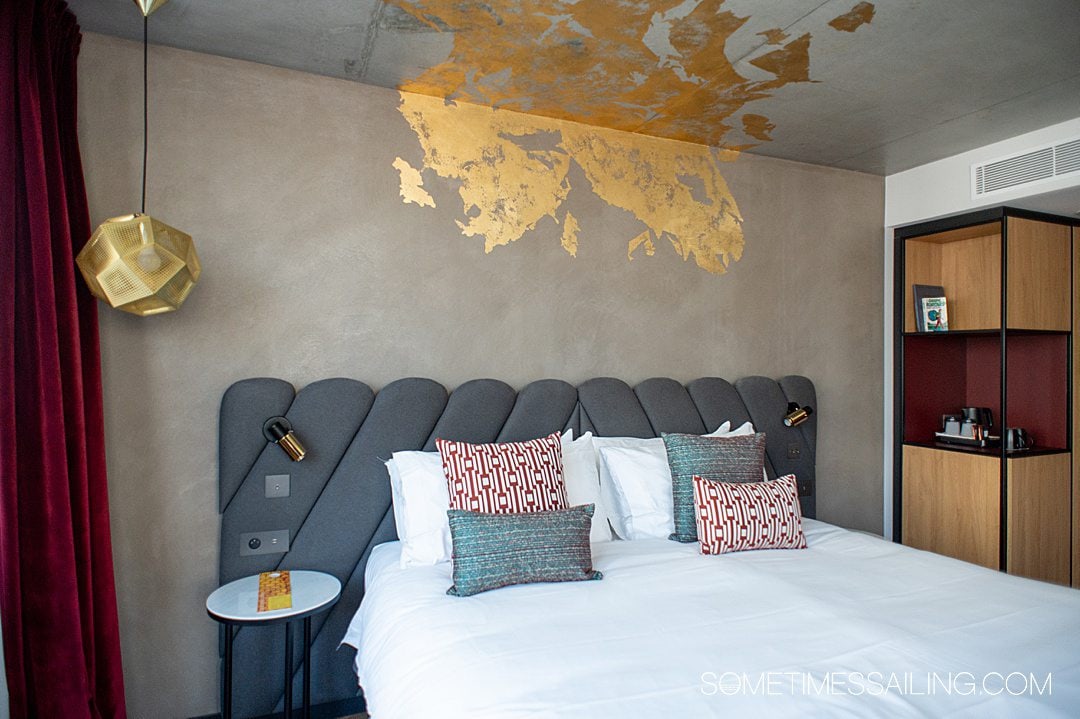 Interior of a hotel room with a queen bed and grey details, with gold foil on the ceiling at The Renaissance hotel in Bordeaux, France.