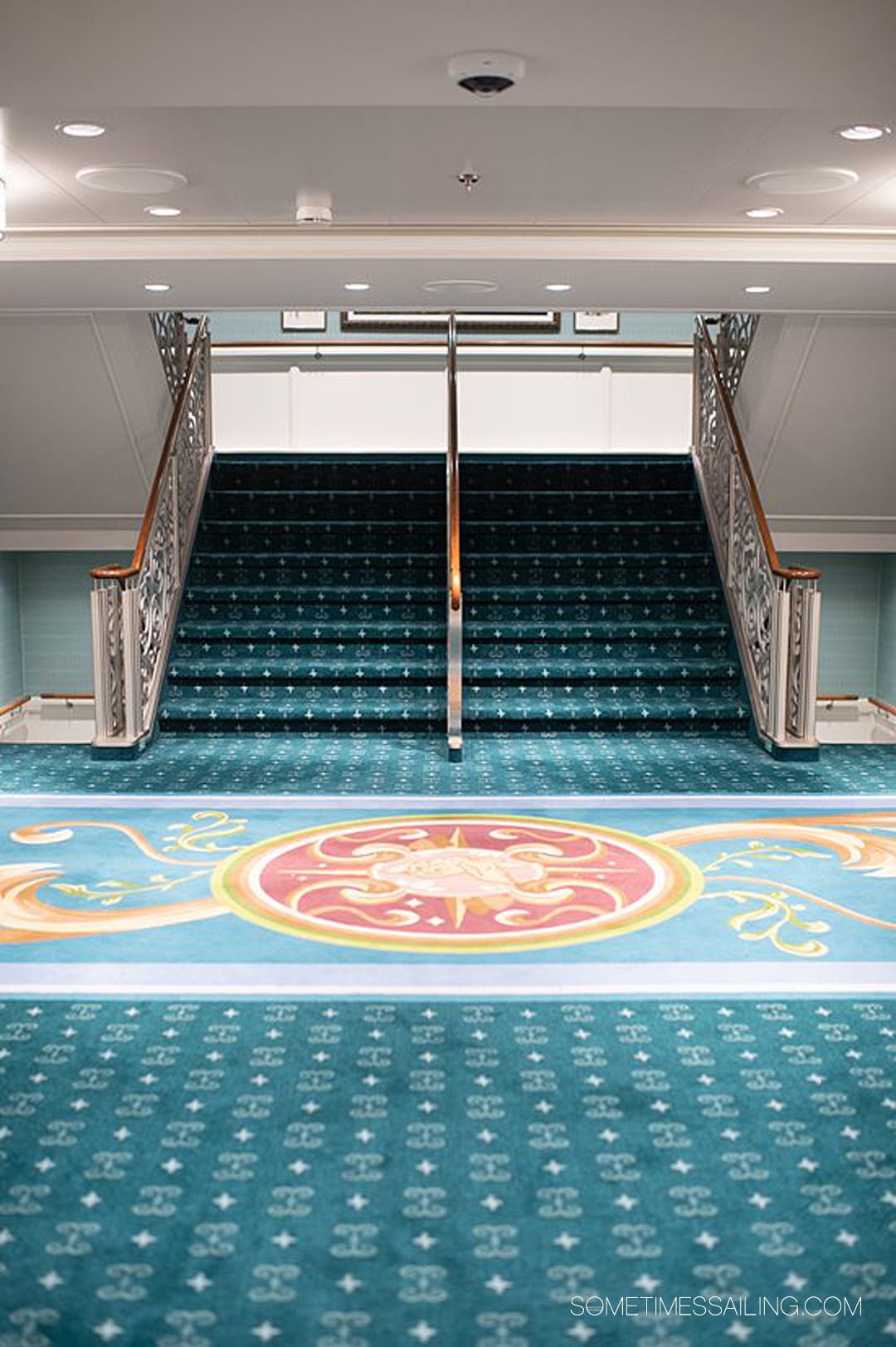 Teal carpet with yellow swirls on Disney Wish next to the stairs.