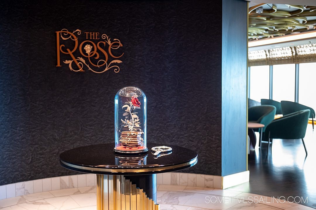 Entrance to The Rose bar on Disney Wish, with a glass encased rose on a black table, with a mirror next to it.