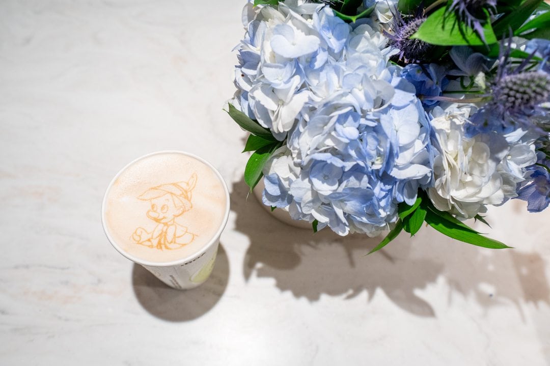 Pinocchio detail and latte art next to blue hydrangea at Wishing Star Cafe on Disney Wish cruise ship.