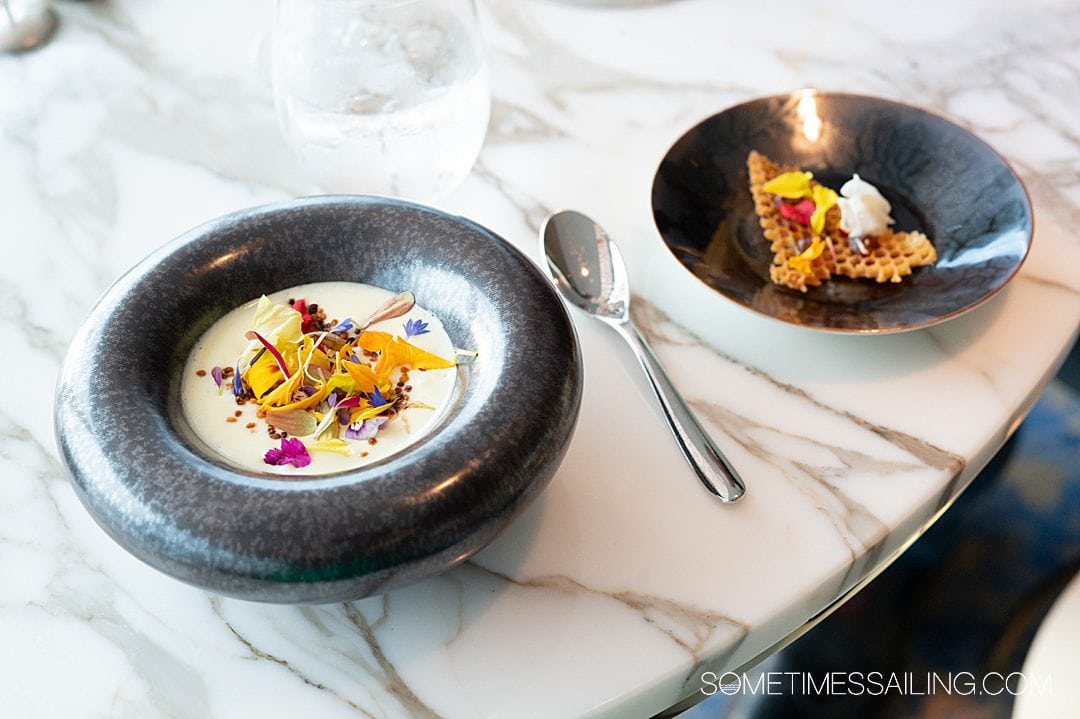 Black bowl on a white marble table with a spoon next to it, with colorful flowers and a honeycomb cracker on top at Enchante on Disney Wish.