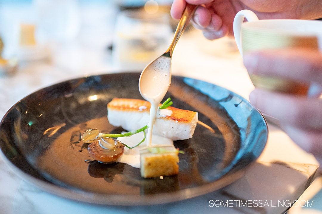 Spoon dripping a sauce over a fish dish at Enchante restaurant on the Disney Wish cruise ship.