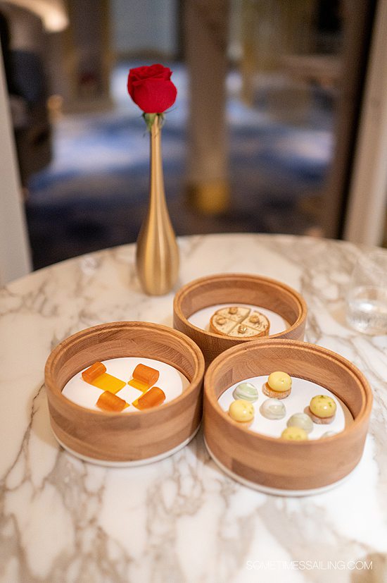 Trio of wooden bowls with desserts in each one, including apricot fruit gels, small half-dome chocolate and a coffee tartlet at Enchante on Disney Wish.