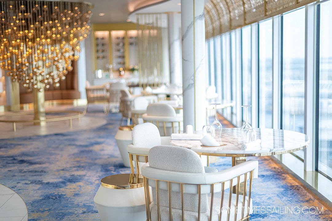 Interior of Enchante restaurant on Disney Wish cruise ship, with blue carpet, white and gold details, and seats facing the cruise ship windows.